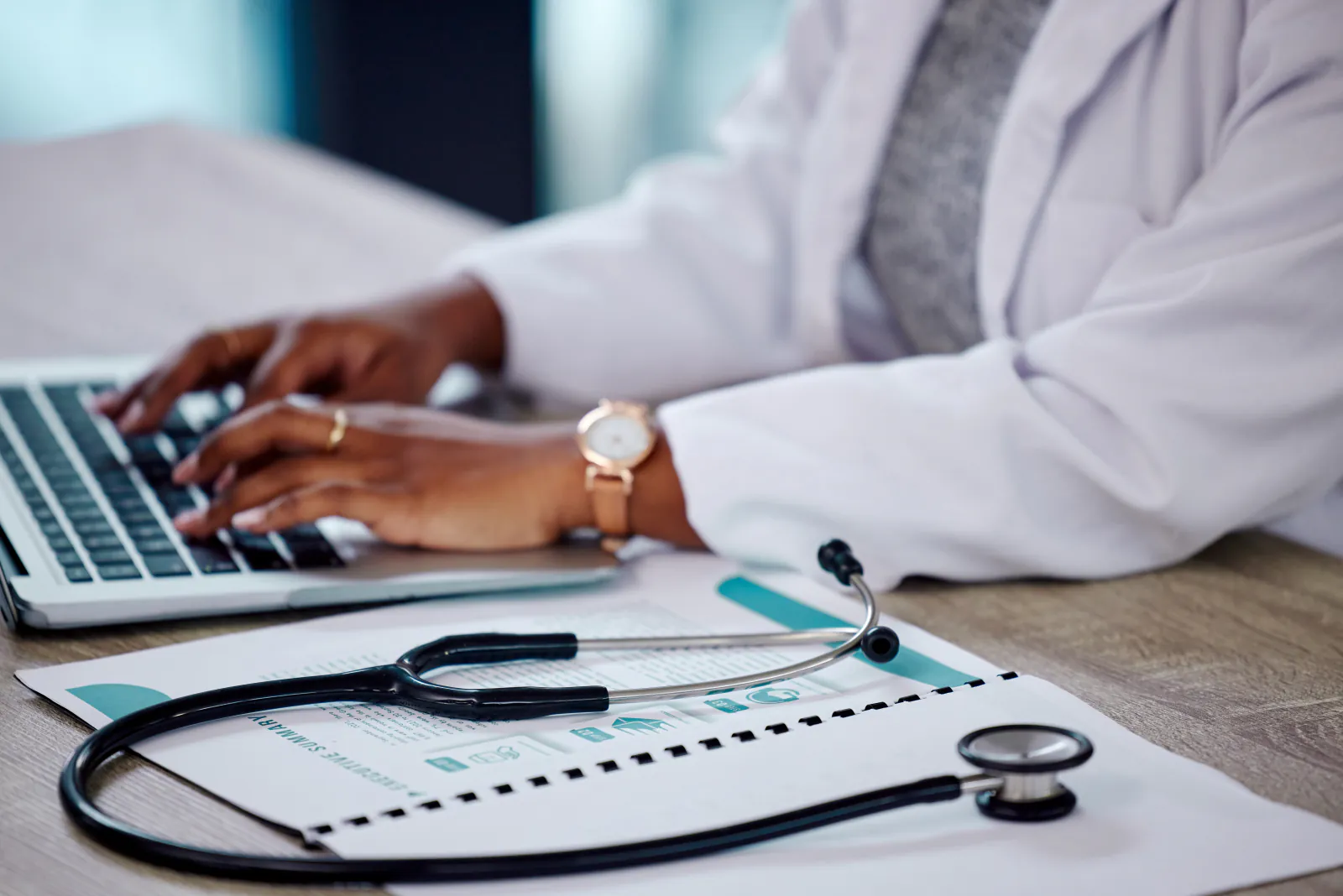 Doctor working on a laptop beside a medical chart and stethoscope